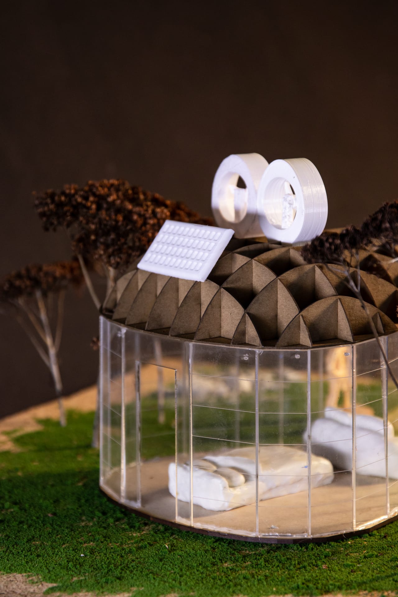 Upright photo of the model pavilion: the ribbed dome with a tilted panel and white fan units, and the glass drum below with a sofa inside