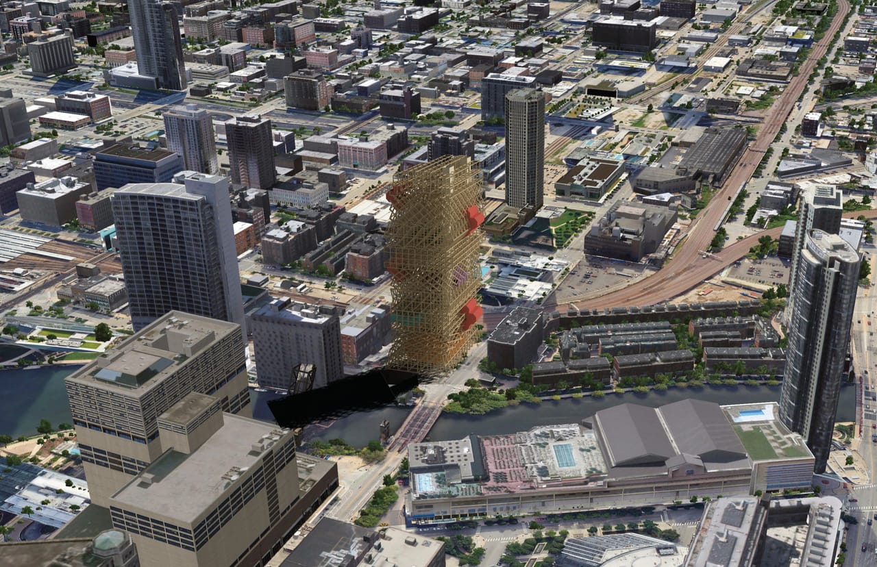 Aerial view of a dense city with a river, railway lines and several tall towers, with the lattice tower placed among them beside the river, its shadow falling across the street