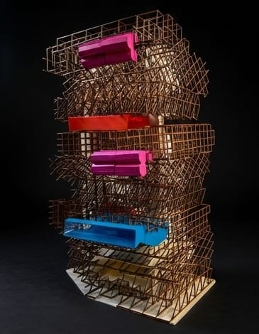 Photograph of the same lattice tower from a closer, slightly turned view, with pink, orange-red and blue volumes set into the frame, against a black background