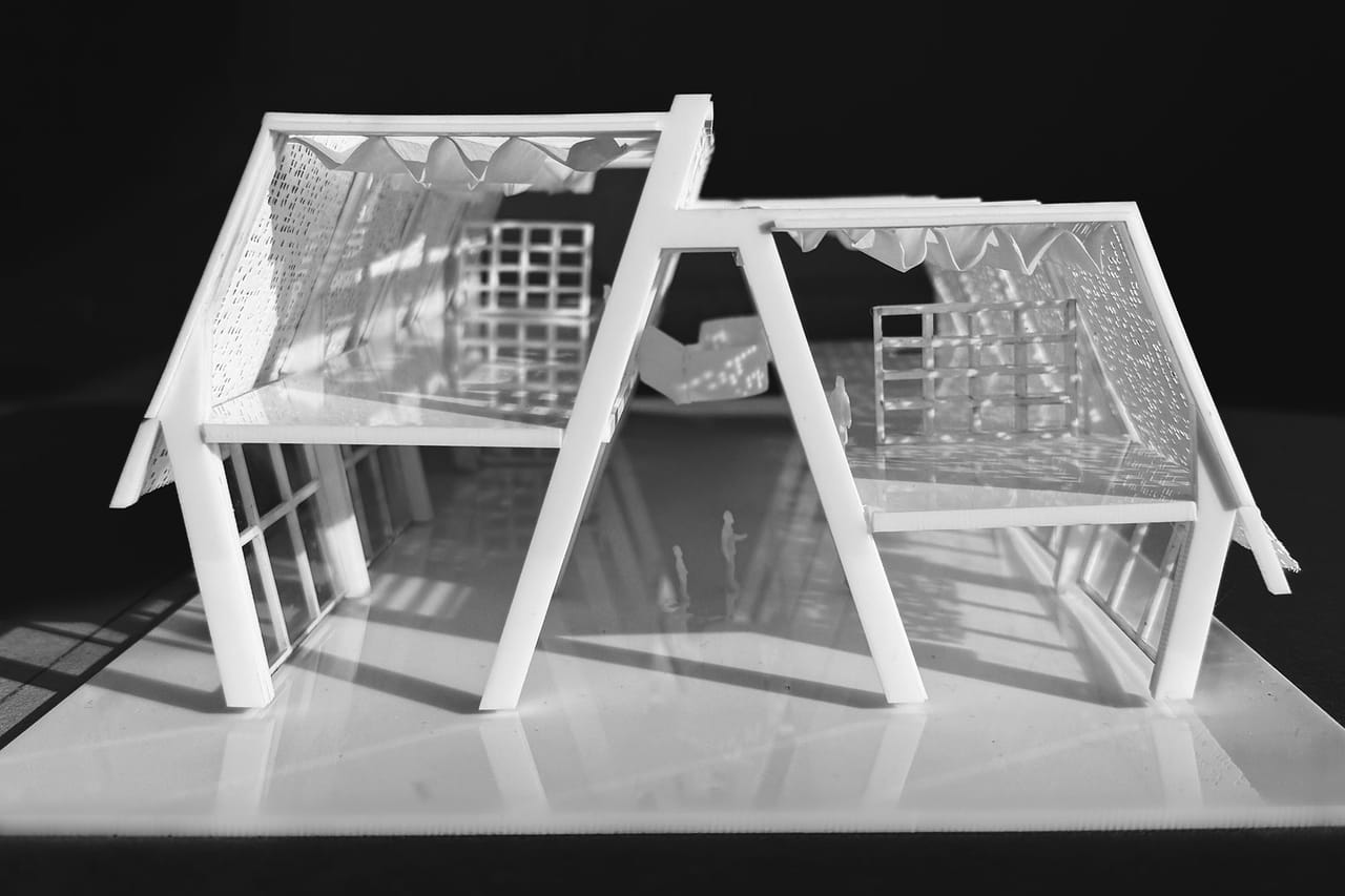 Black-and-white photograph of a white study model cut open through two A-shaped frames, showing a grid of shelves and a wavy fabric roof